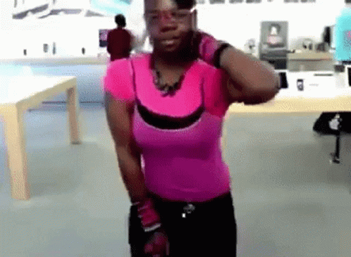 A Woman In A Pink Shirt Is Standing In Front Of A Table GIF