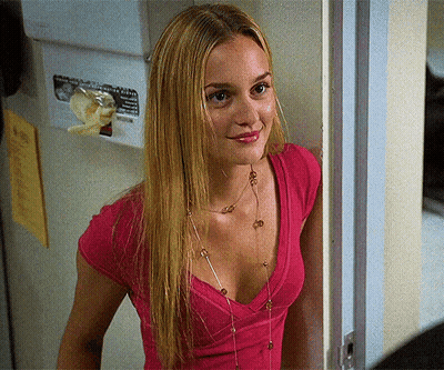 A Woman In A Pink Shirt Is Standing In Front Of A Wall With A Sign That Says " No Smoking " GIF