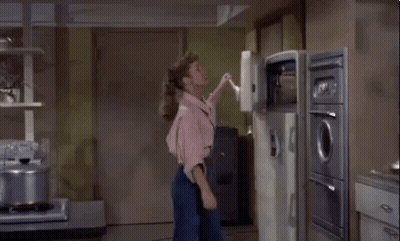 A Woman In A Pink Shirt Is Standing In Front Of An Open Refrigerator In A Kitchen GIF