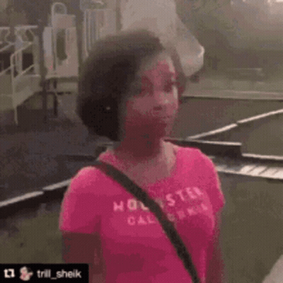 A Woman In A Pink Shirt Is Standing On A Sidewalk With A Bicycle In The Background And Says Do You Wanna Fight ? GIF