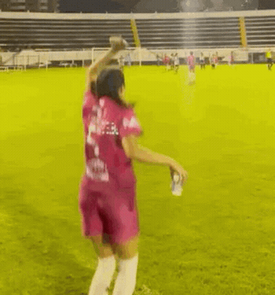A Woman In A Pink Shirt Is Standing On A Soccer Field With Another Woman . GIF