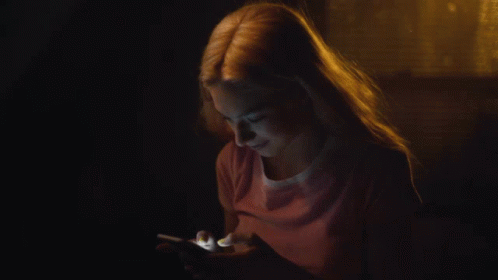 A Woman In A Pink Shirt Is Using A Cell Phone In The Dark GIF