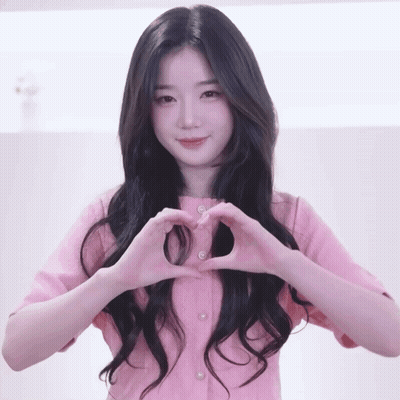 A Woman In A Pink Shirt Making A Heart Shape With Her Hands GIF
