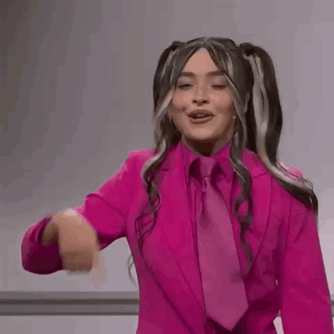 A Woman In A Pink Suit And Tie Is Dancing And Pointing At The Camera . GIF