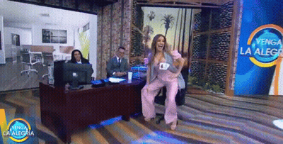 A Woman In A Pink Suit Is Dancing In Front Of A Sign That Says " Venga La Alegria " GIF