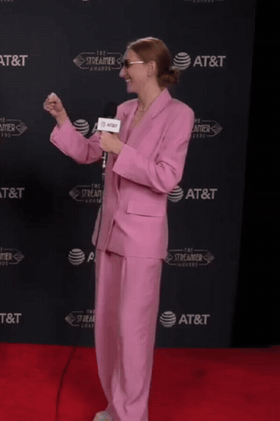 A Woman In A Pink Suit Is Holding A Microphone In Front Of An At & T Wall GIF