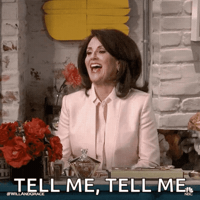 A Woman In A Pink Suit Is Sitting At A Table Laughing And Saying `` Tell Me , Tell Me '' . GIF