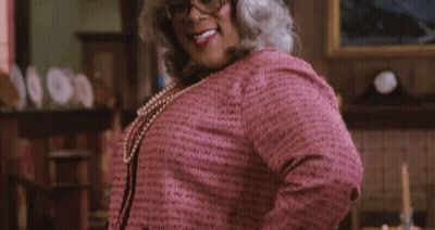 A Woman In A Pink Sweater And Pearls Is Smiling With Her Tongue Out GIF