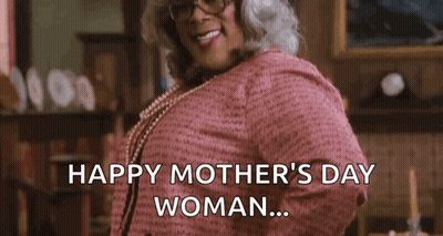 A Woman In A Pink Sweater And Pearls Is Standing In A Living Room . GIF