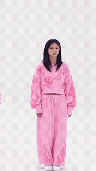 A Woman In A Pink Sweater And Pink Sweatpants Is Standing In Front Of A White Background . GIF