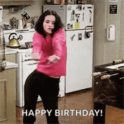 A Woman In A Pink Sweater Is Dancing In A Kitchen With The Words `` Happy Birthday '' Written Below Her . GIF