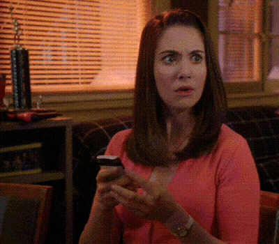 A Woman In A Pink Sweater Is Looking At Her Cell Phone GIF