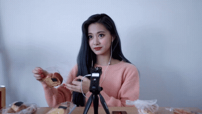 A Woman In A Pink Sweater Is Sitting At A Table Eating Food GIF