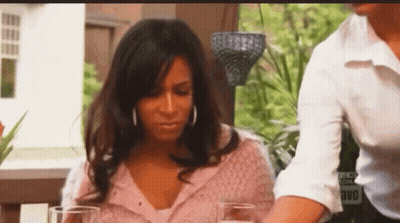 A Woman In A Pink Sweater Is Sitting At A Table With A Man And Two Glasses Of Wine . GIF