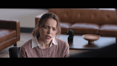 A Woman In A Pink Sweater Is Sitting In Front Of A Couch GIF