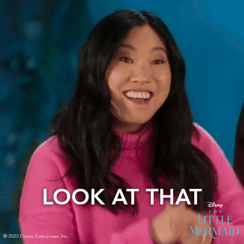 A Woman In A Pink Sweater Is Smiling With The Words Look At That Behind Her GIF
