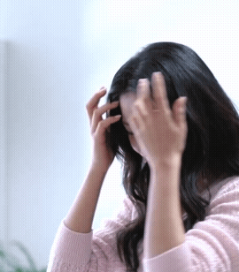 A Woman In A Pink Sweater Is Touching Her Hair With Her Hands GIF