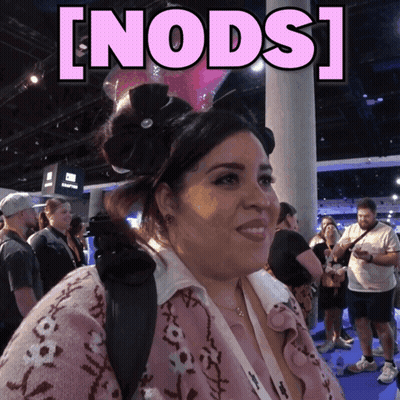 A Woman In A Pink Sweater Stands In Front Of A Sign That Says ' Nods ' GIF