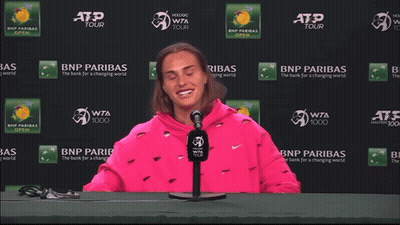 A Woman In A Pink Sweatshirt Is Sitting In Front Of A Bnp Paribas Sign GIF