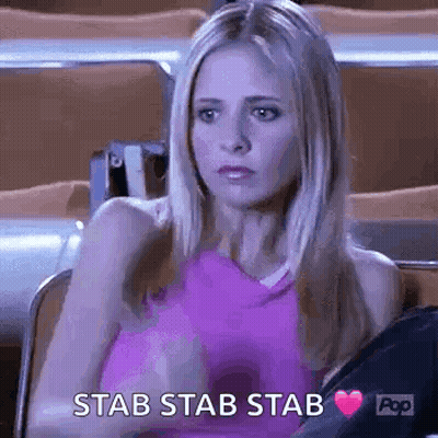 A Woman In A Pink Tank Top Is Sitting In A Stadium With A Heart In Her Hand And The Words `` Stab Stab Stab '' . GIF