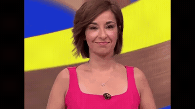 A Woman In A Pink Tank Top Is Smiling While Standing In Front Of A Yellow And Blue Background . GIF
