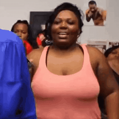 A Woman In A Pink Tank Top Is Standing In Front Of A Group Of People In A Room . GIF