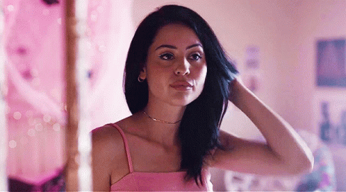 A Woman In A Pink Tank Top Is Standing In Front Of A Mirror . GIF