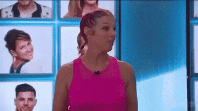 A Woman In A Pink Tank Top Is Standing In Front Of A Wall Of Portraits Of People . GIF
