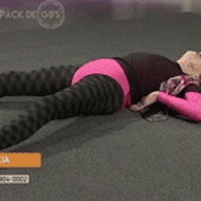 A Woman In A Pink Top And Black Pants Is Laying On The Floor Stretching Her Legs GIF