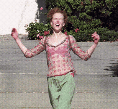 A Woman In A Pink Top And Green Pants Is Screaming With Her Arms In The Air GIF