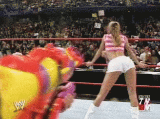 A Woman In A Pink Top And White Shorts Is Dancing In A Wrestling Ring With A Wwe Logo In The Background GIF