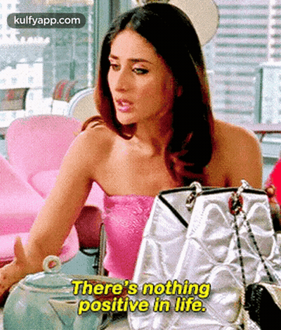 A Woman In A Pink Top Is Sitting At A Table With Handbags And Says `` There 'S Nothing Positive In Life '' . GIF