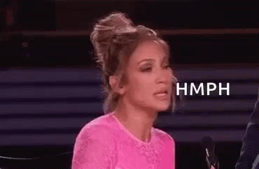 A Woman In A Pink Top Is Sitting In Front Of A Microphone And Making A Funny Face . GIF