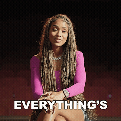 A Woman In A Pink Top Is Sitting With Her Legs Crossed And The Words Everything 'S Behind Her GIF