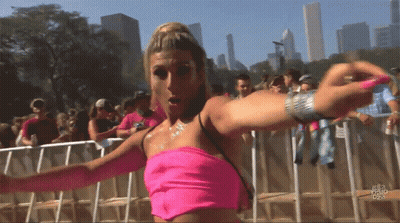 A Woman In A Pink Top Stands In Front Of A Crowd At A Festival GIF