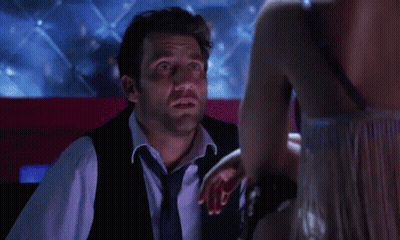 A Woman In A Pink Wig Is Smiling At A Man In Front Of A Red Curtain . GIF
