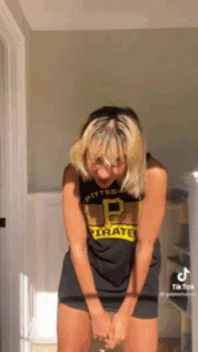 A Woman In A Pittsburgh Pirates Shirt Is Standing In A Room With Her Hands On Her Knees . GIF