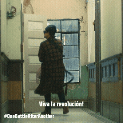 A Woman In A Plaid Coat Is Walking Down A Hallway With The Words Viva La Revolucion On The Bottom GIF