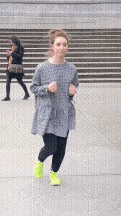 A Woman In A Plaid Dress And Neon Yellow Shoes Is Running Down The Street GIF