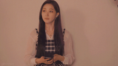 A Woman In A Plaid Dress Is Standing In Front Of A White Wall GIF