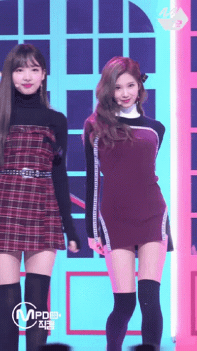 A Woman In A Plaid Dress Is Standing Next To Another Woman In A Black Dress GIF