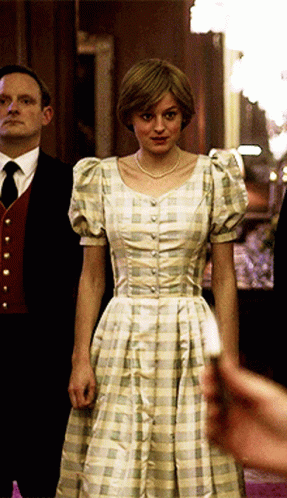 A Woman In A Plaid Dress Stands In Front Of A Man In A Suit And Tie GIF