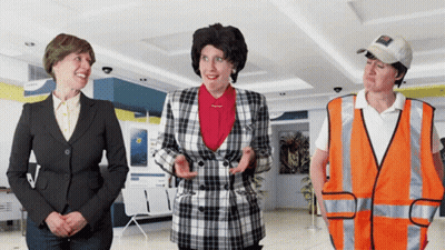 A Woman In A Plaid Jacket Stands Next To Two Other Women GIF
