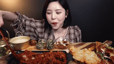 A Woman In A Plaid Shirt Is Sitting At A Table Eating Food . GIF