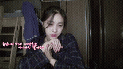 A Woman In A Plaid Shirt Is Sitting In A Room With Korean Writing On The Walls GIF