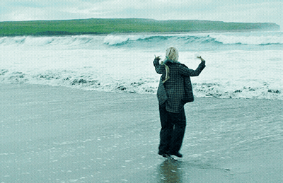 A Woman In A Plaid Shirt Is Standing On A Beach GIF