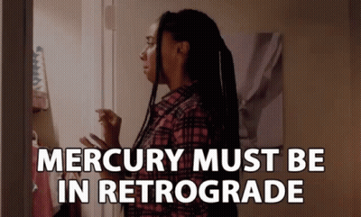 A Woman In A Plaid Shirt Stands In Front Of A Door With The Words " Mercury Must Be In Retrograde " GIF