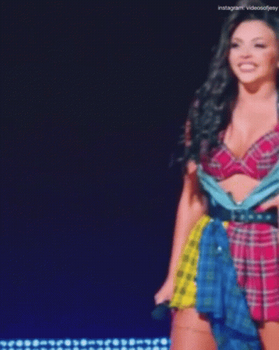 A Woman In A Plaid Top And Skirt Is Standing On A Stage . GIF