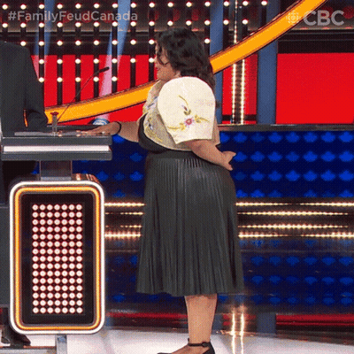 A Woman In A Pleated Skirt Stands On A Stage In Front Of A Sign That Says ' Family Feud Canada ' On It GIF