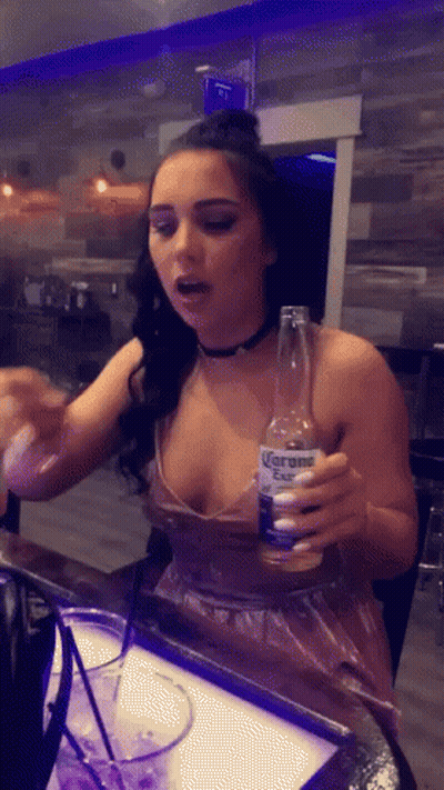 A Woman In A Plunging Neckline Holds A Bottle Of Corona GIF
